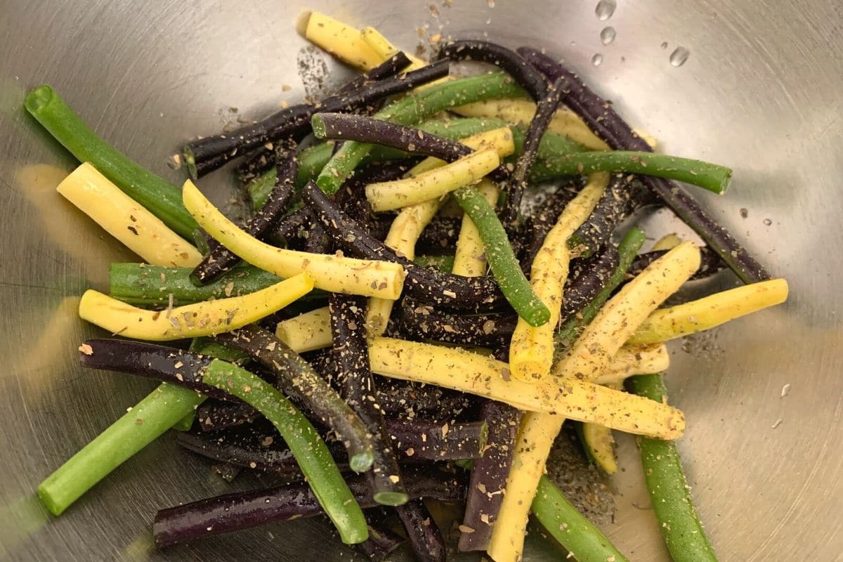 Raw green beans and seasonings in a large bowl.