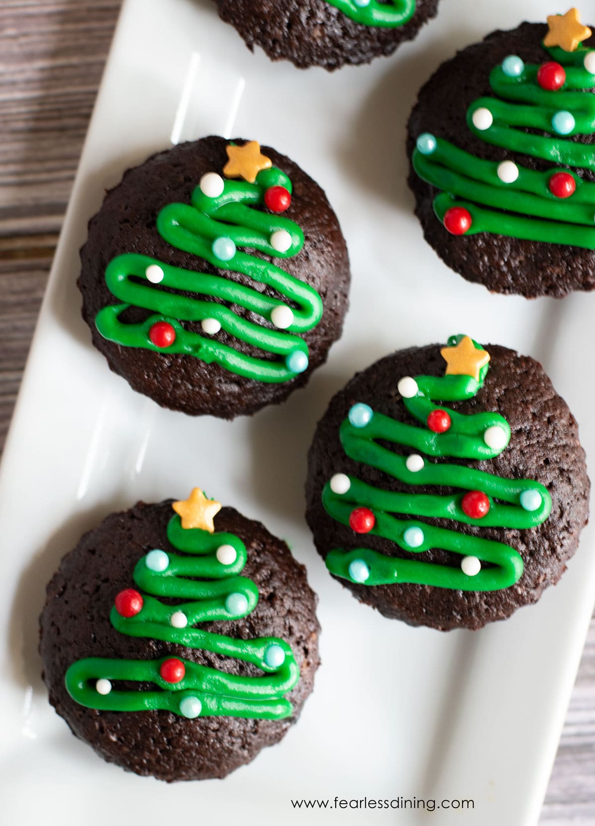 Gluten free brownie bites decorated with icing Christmas trees on a platter.