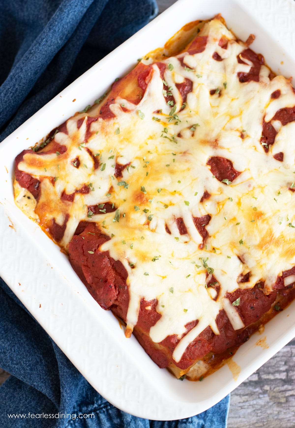 An 8x8 white baking dish filled with baked manicotti.