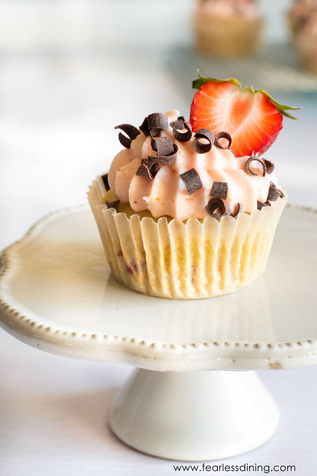 A frosted strawberry cupcake on a white cupcake stand.