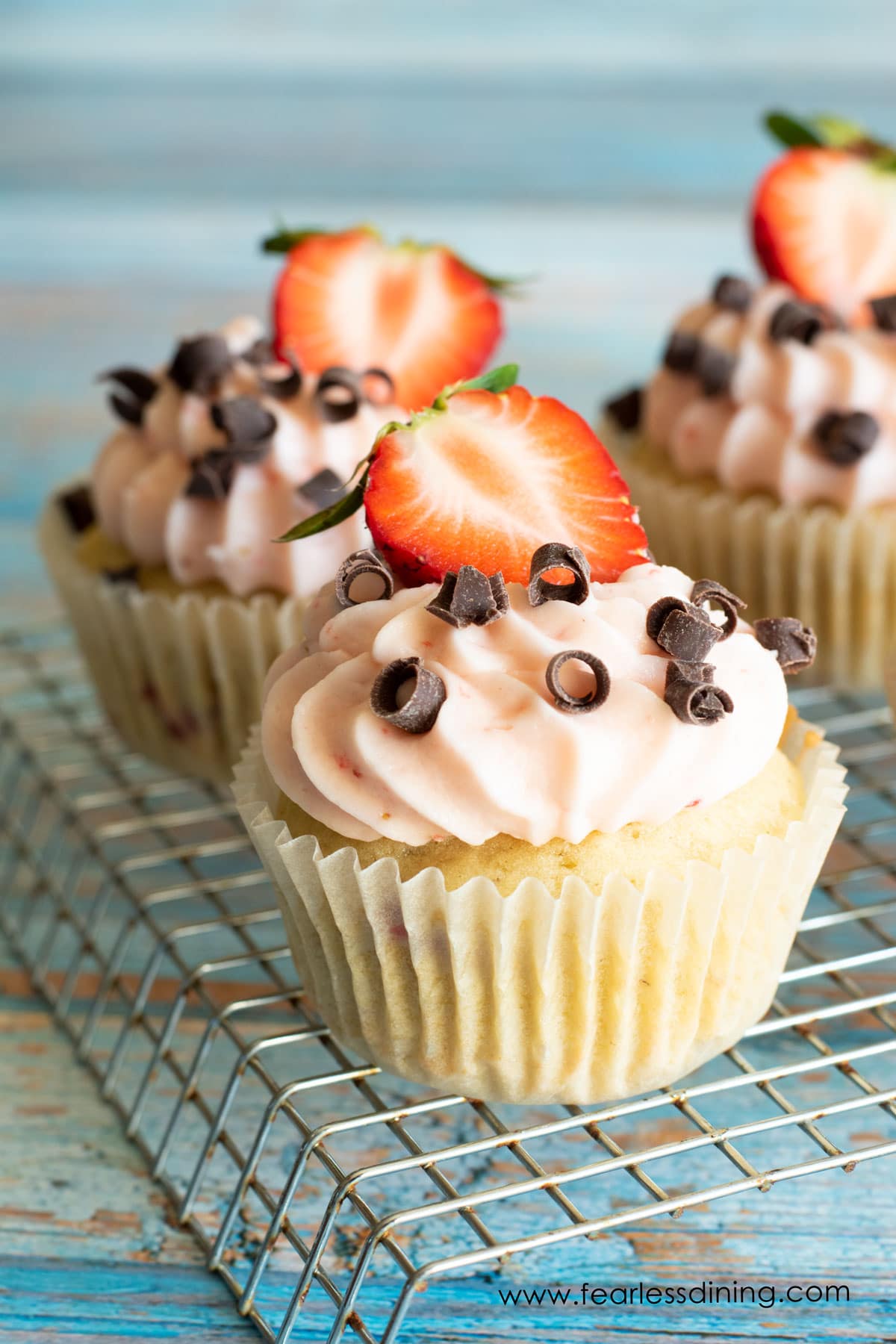 Frosted gluten free strawberry cupcakes on a rack.