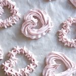 strawberry meringues piped into heart shapes on a baking sheet