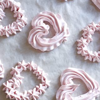 Rows of strawberry meringues piped into heart shapes on a baking sheet.