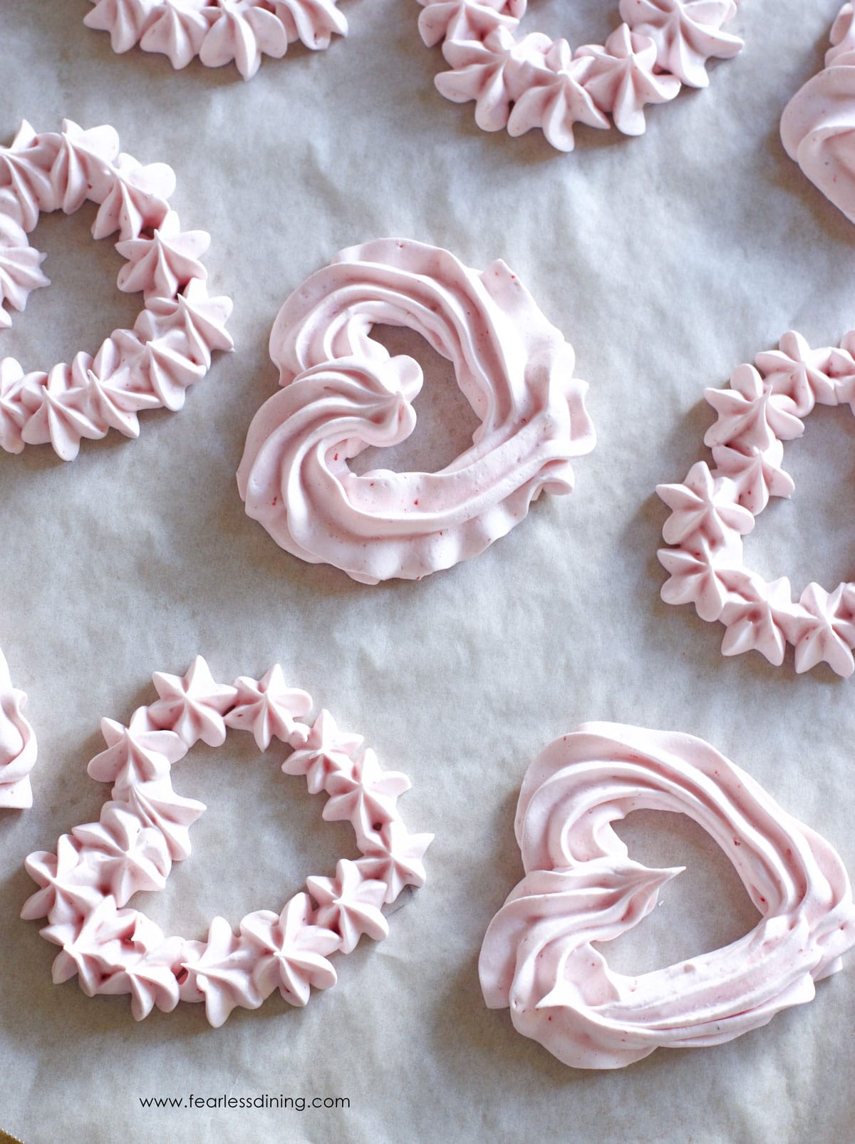 Strawberry meringues piped into heart shapes on a baking sheet.