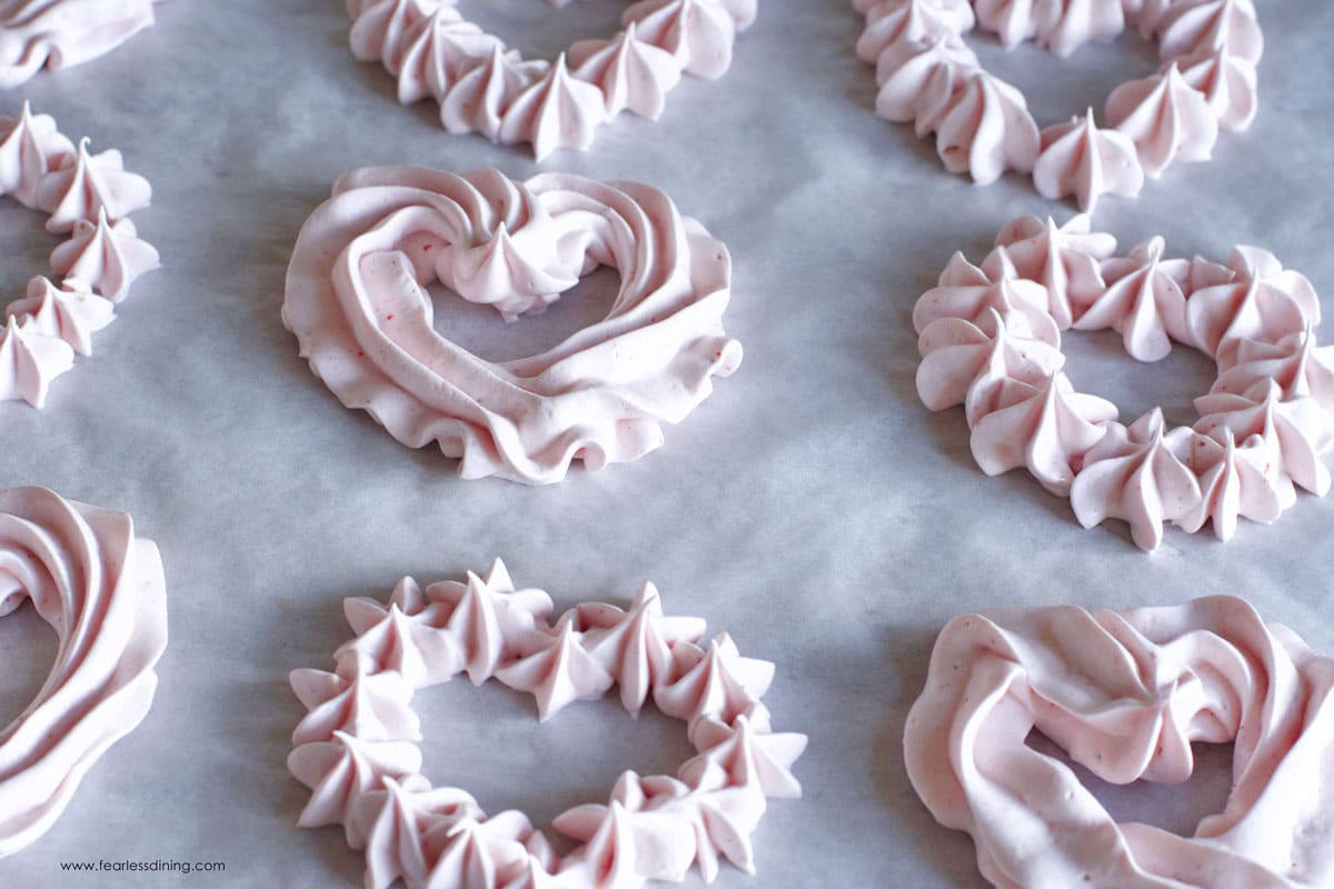 Baked strawberry meringue hearts on a baking sheet.