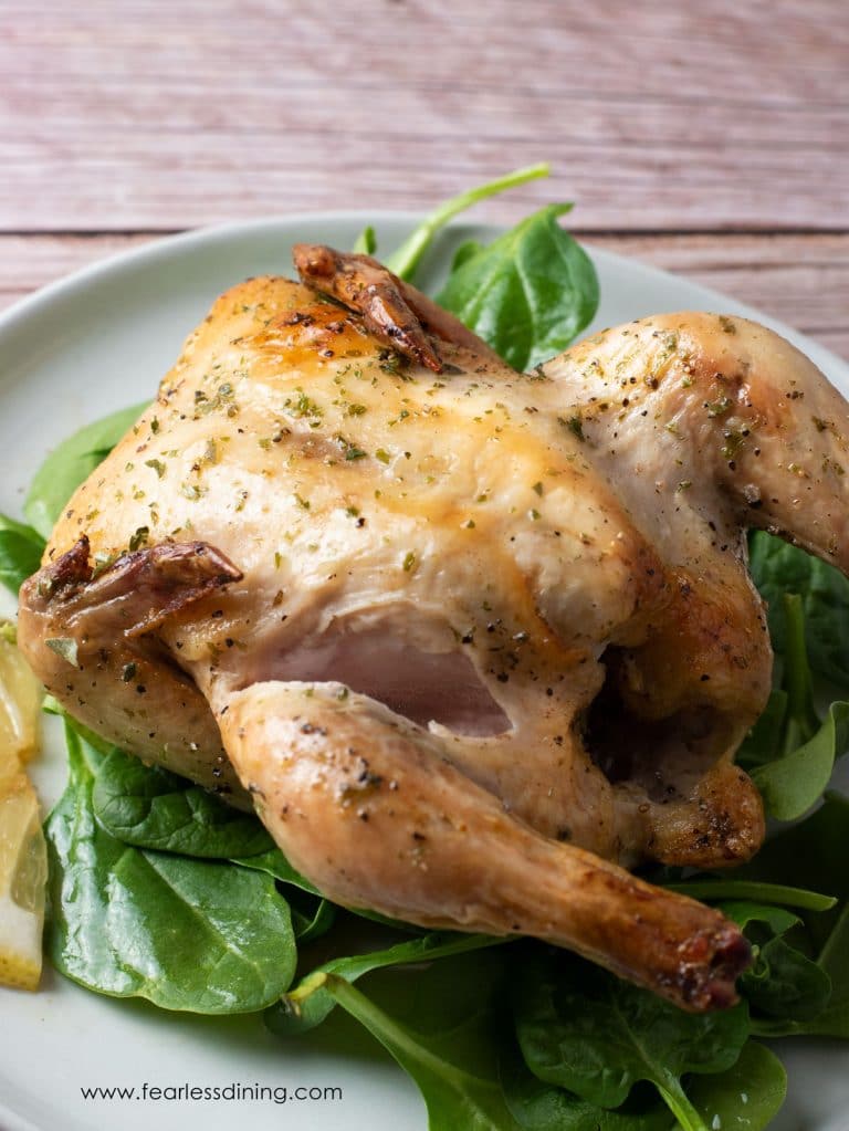 A roasted lemon pepper Cornish game hen on a bed of spinach.
