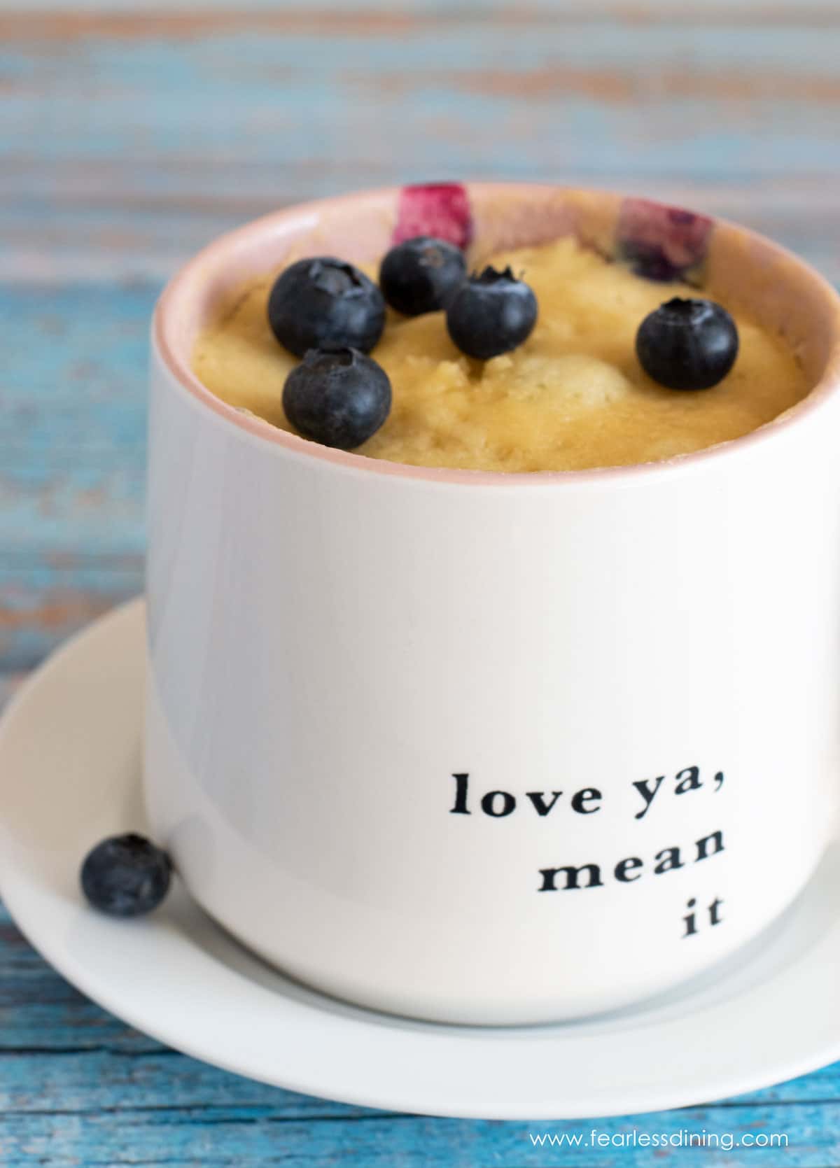 A cooked blueberry mug muffin in a mug topped with blueberries.