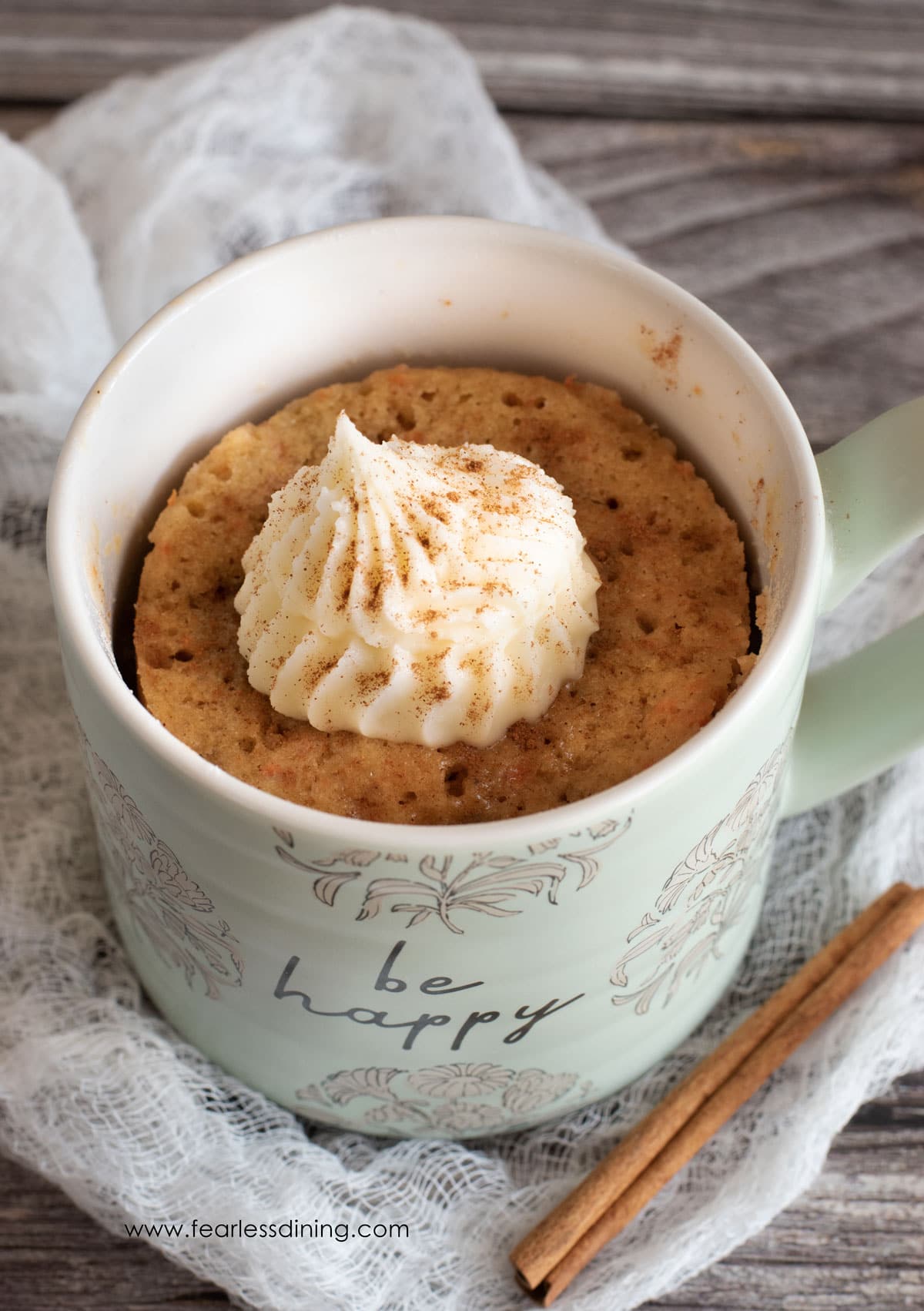 A cooked carrot cake in a mug with a dollop of frosting.