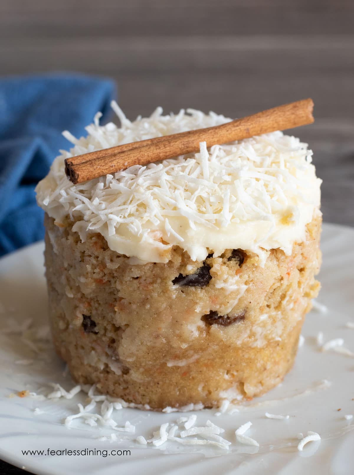 A carrot mug cake on a plate with frosting and shredded coconut on top.