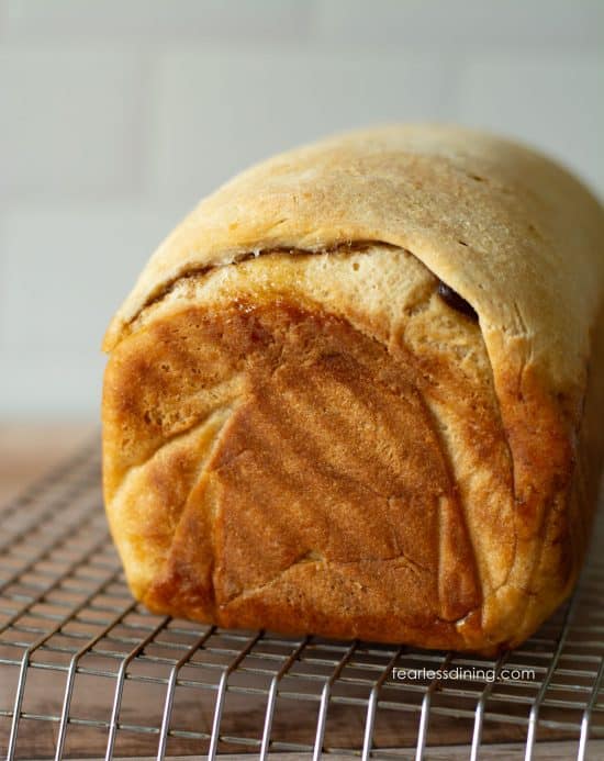 A baked loaf of gluten-free cinnamon raisin bread on a cooling rack.