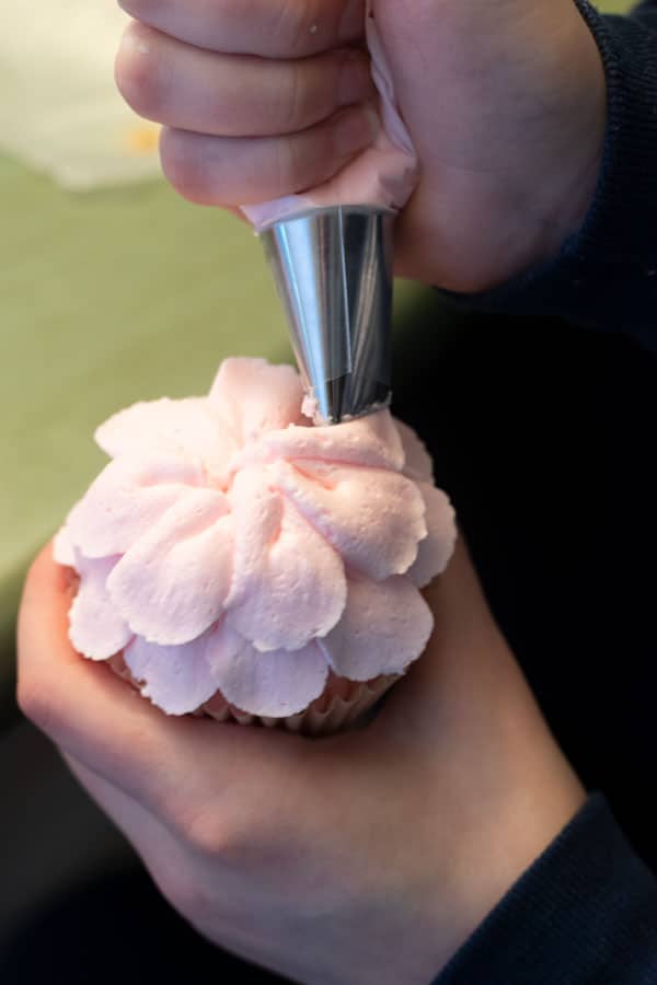 Piping a pink frosting flower onto a cupcake