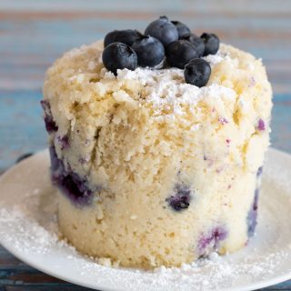A gluten free blueberry mug muffin on a plate. It is topped with fresh blueberries.