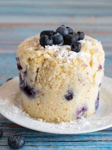A gluten free blueberry mug muffin on a plate. It is topped with fresh blueberries.