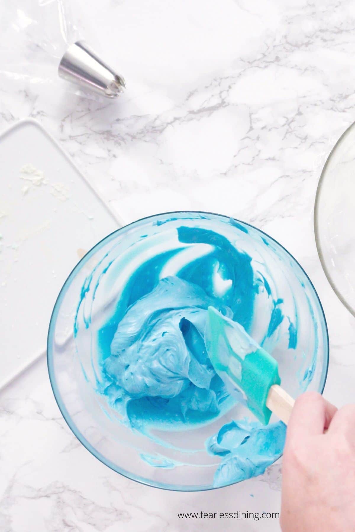 Stirring blue frosting in a glass bowl.
