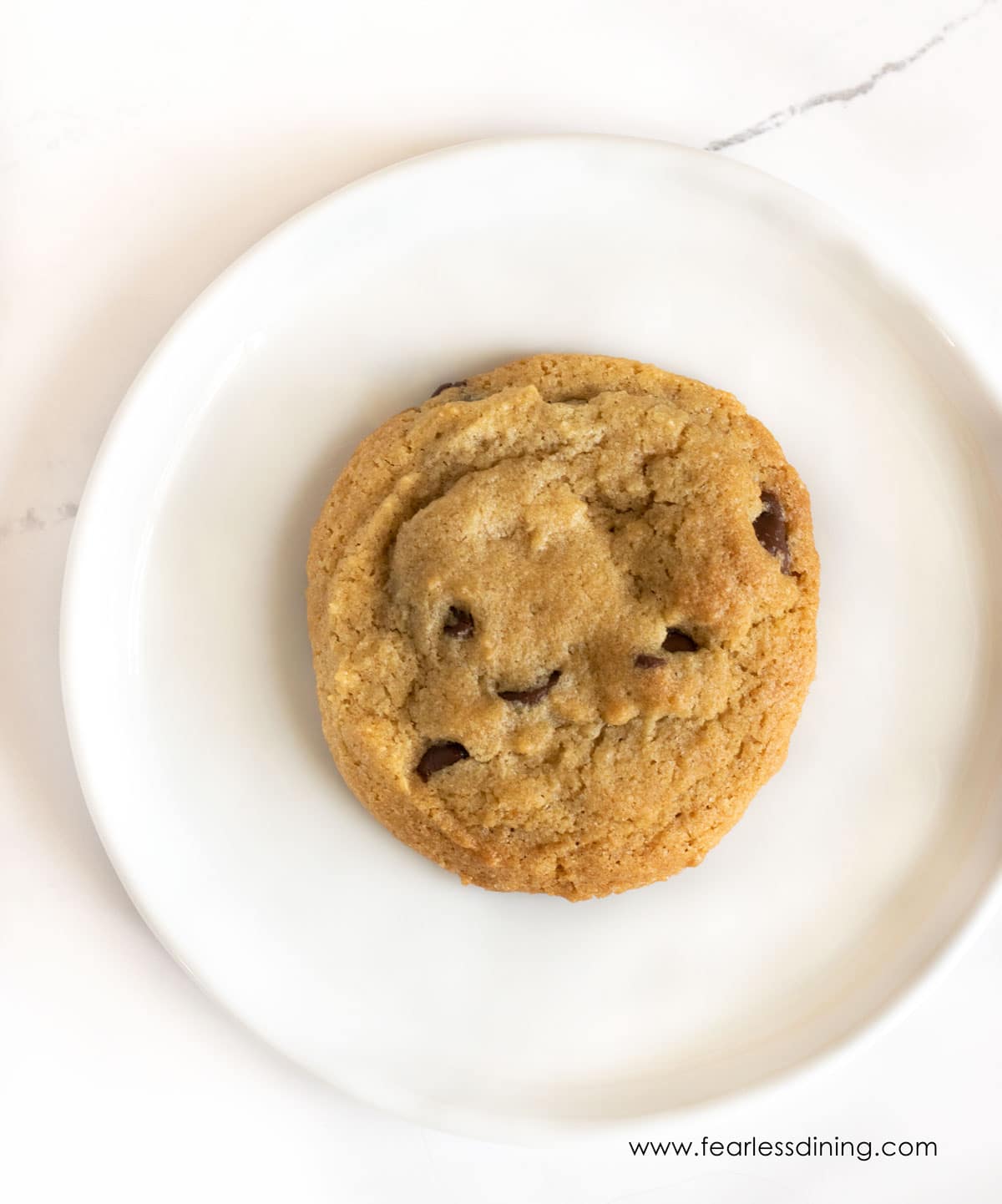 A large Toll House cookie on a white plate.