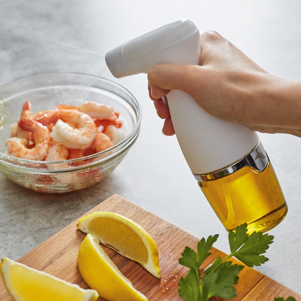 An oil mister ready to spray shrimp that is in a bowl.
