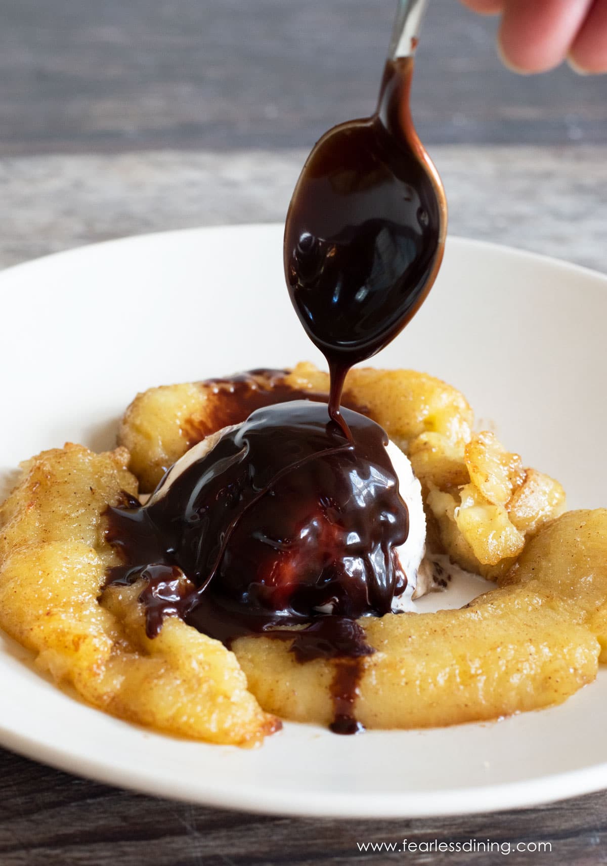 Drizzling hot fudge over caramelized air fryer bananas and ice cream.