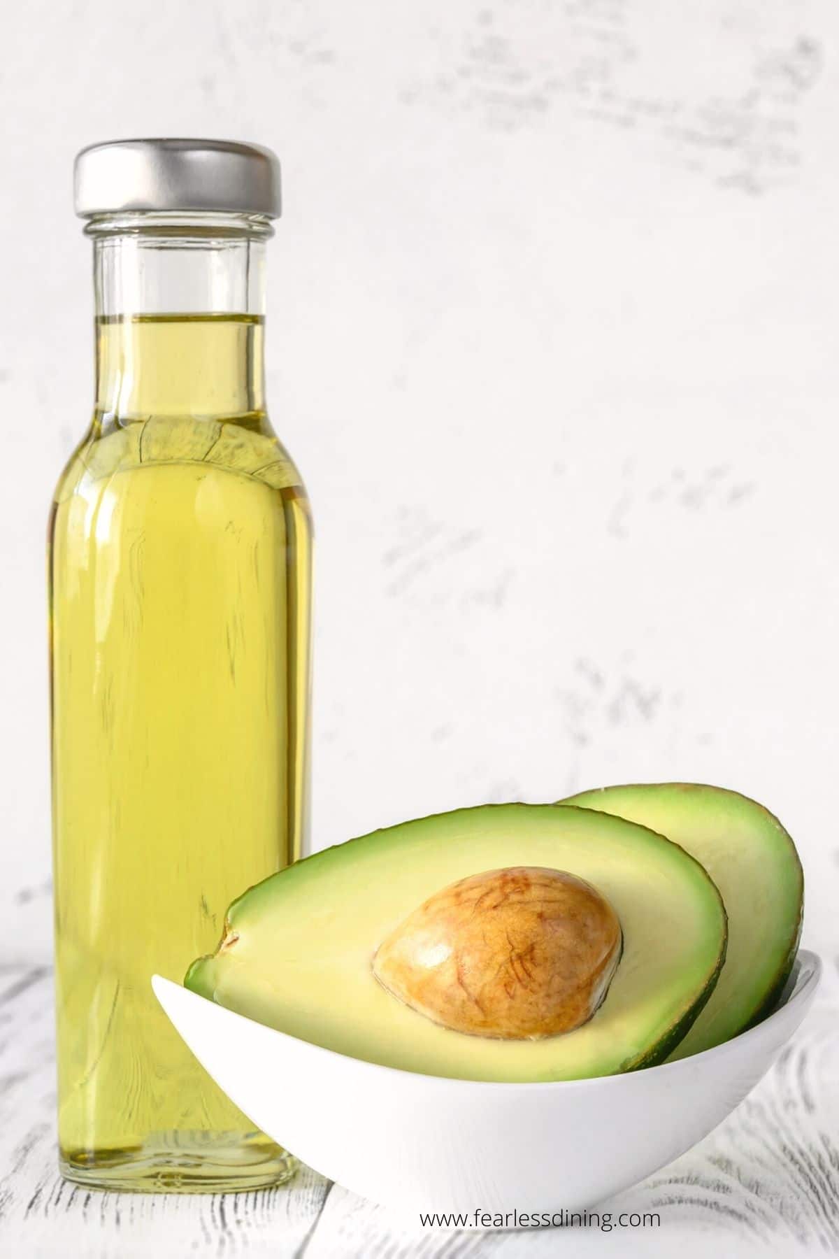 A bottle of avocado oil next to a bowl of avocados.