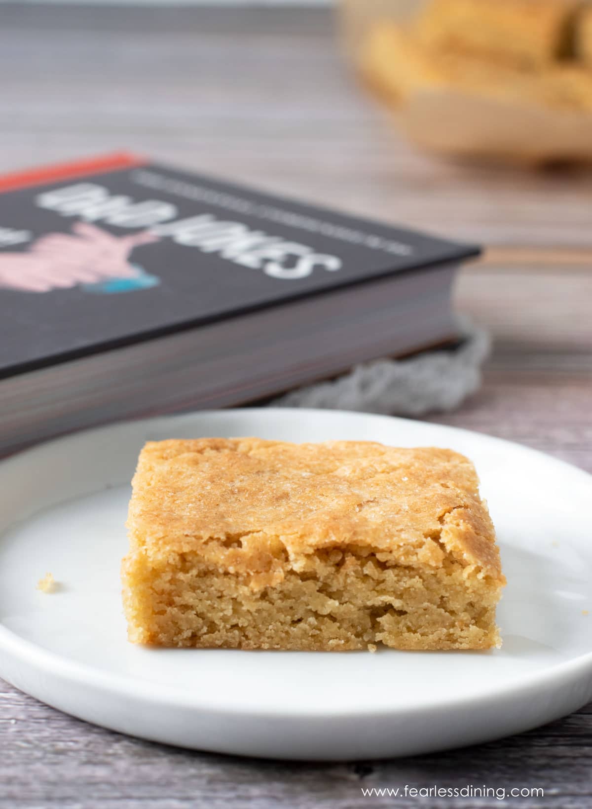 A butterscotch brownie on a plate next to a dad joke book.