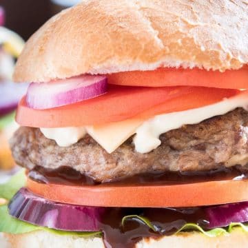 A hamburger with onion, tomato, cheese, and barbecue sauce on a gluten free hamburger bun.