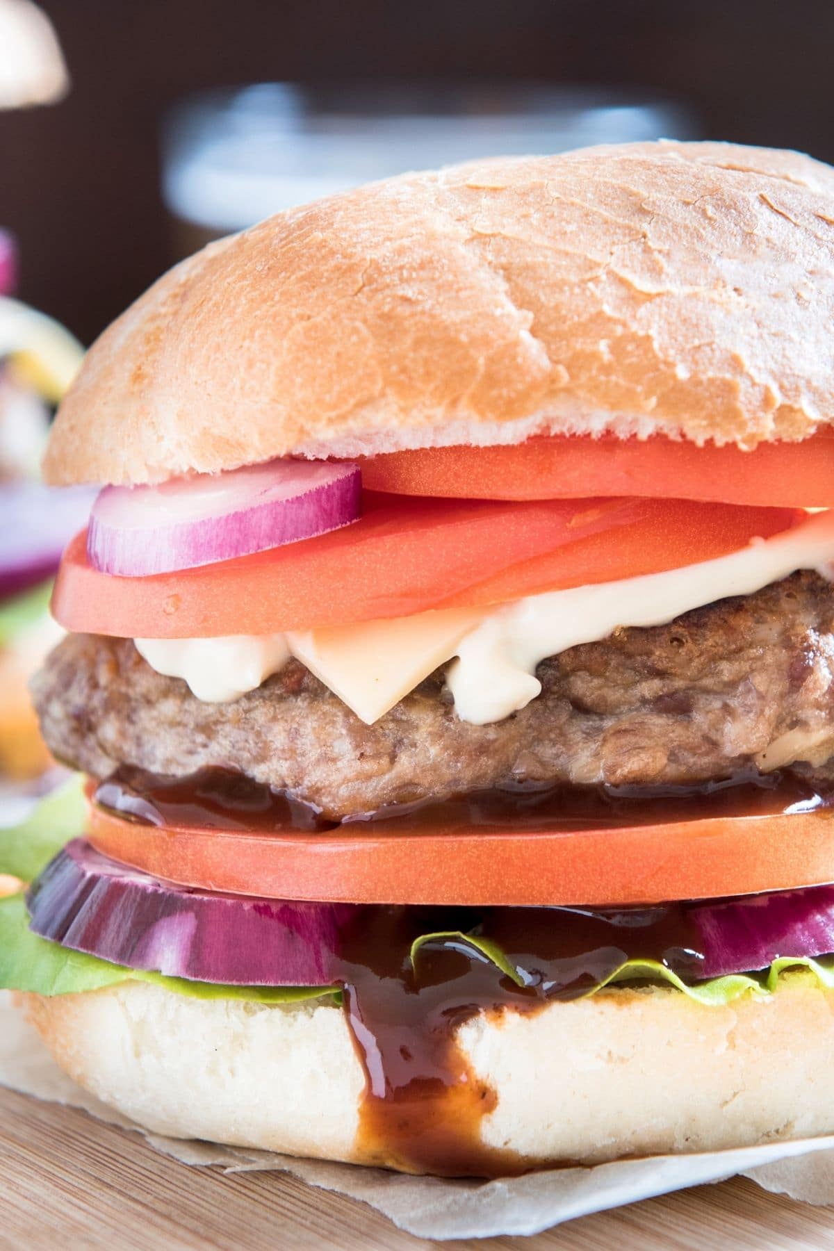 A hamburger with onion, tomato, cheese, and barbecue sauce on a gluten free hamburger bun.