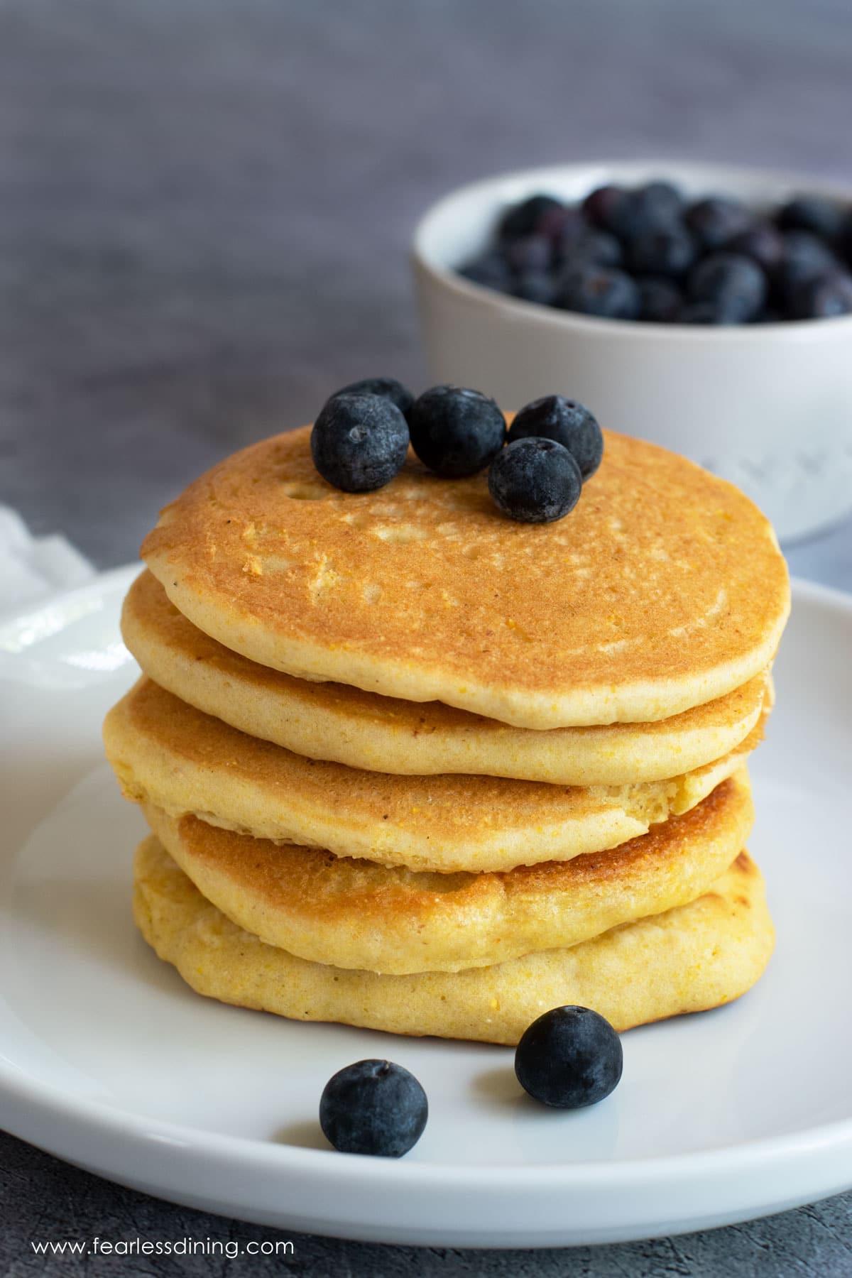 A stack of five cornmeal pancakes topped with fresh blueberries.