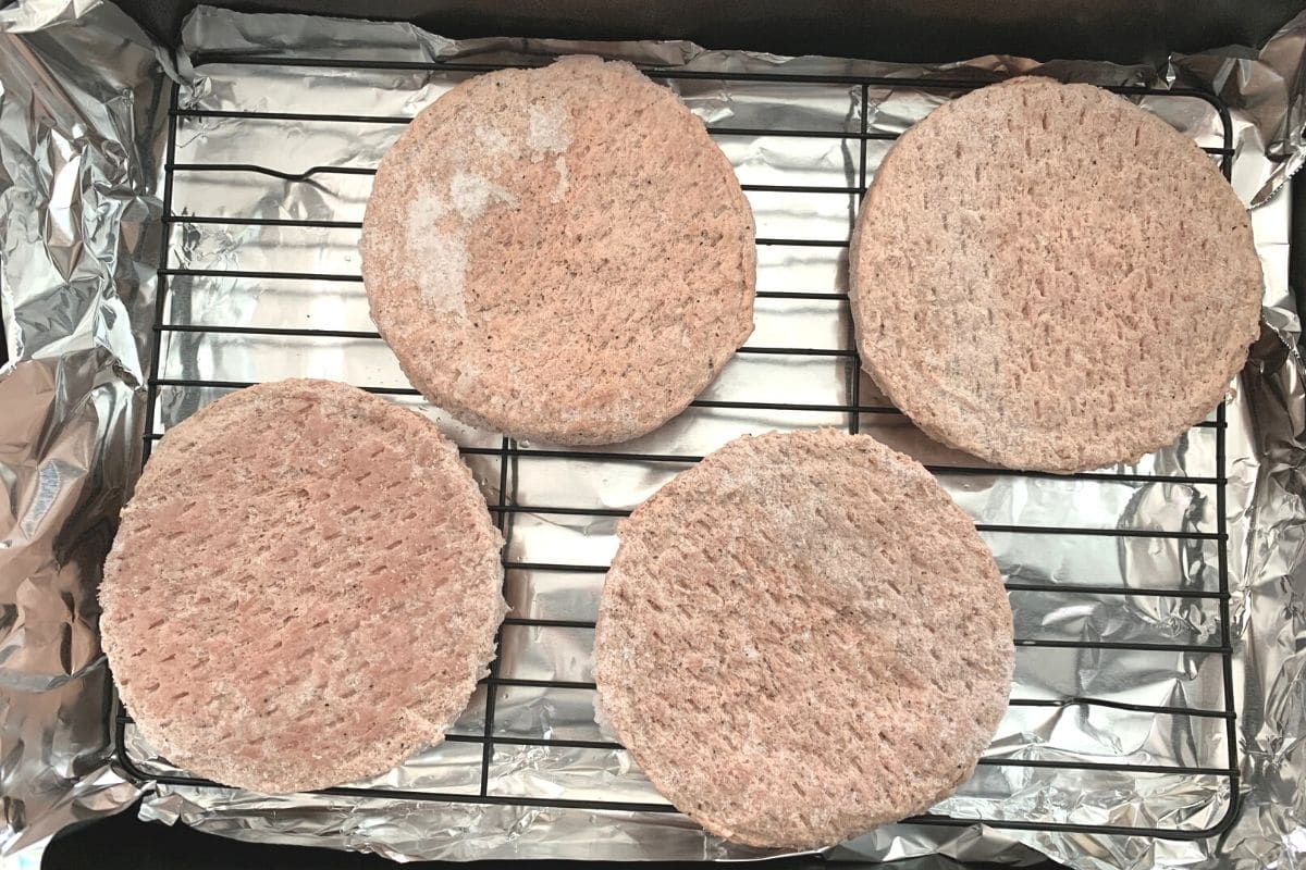 Frozen turkey burger patties on a wire rack in a roasting pan.