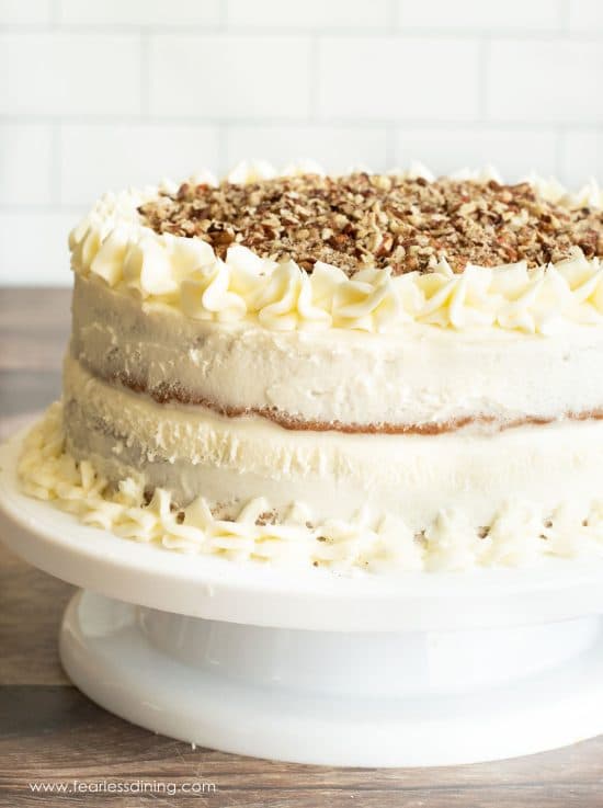 A frosted gluten free hummingbird cake on a white cake stand.