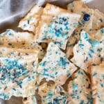 A Pinterest image of white chocolate covered matzo bark that is decorated with blue sprinkles.