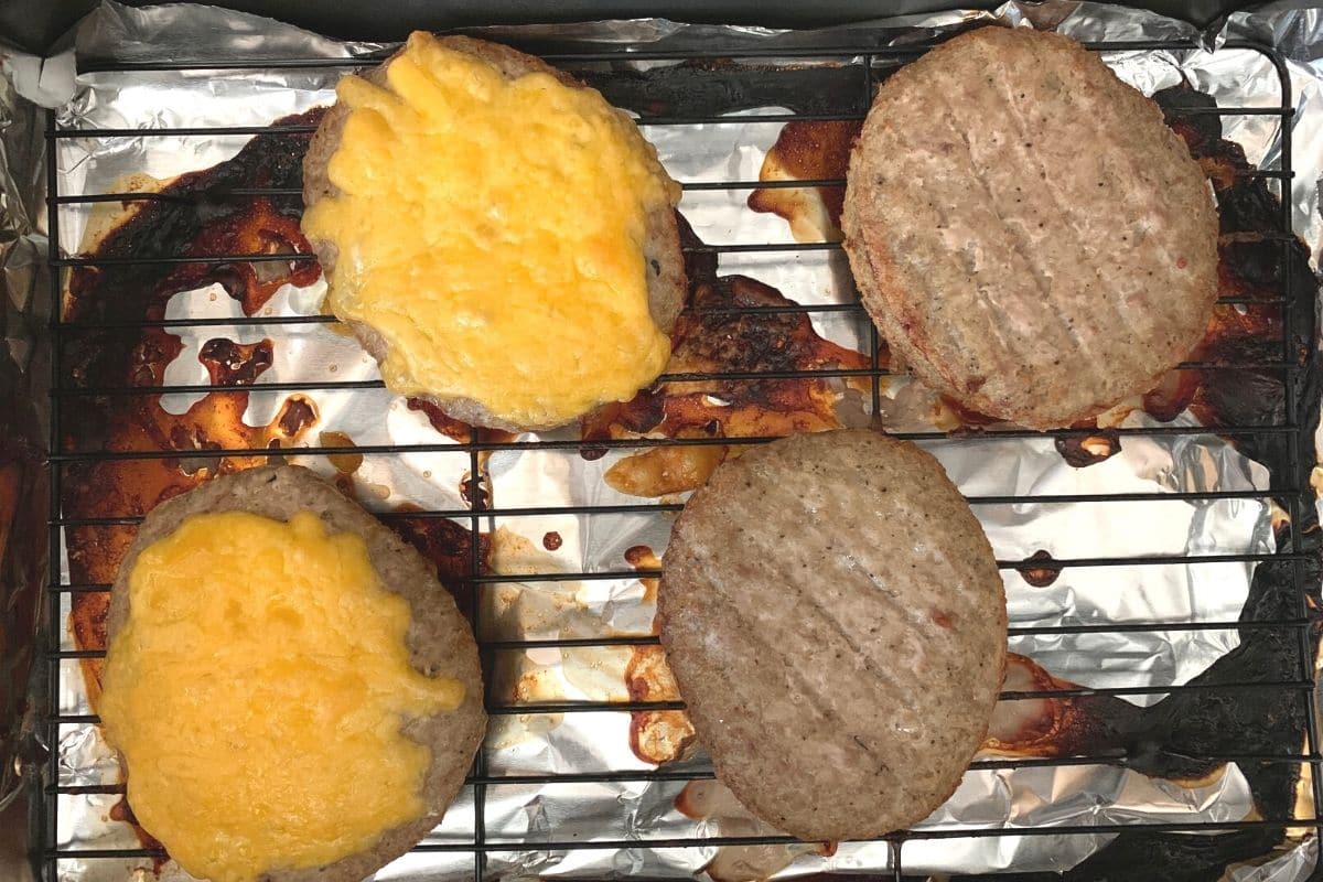 Cooked burgers on the wire rack. Two burgers have melted cheese.