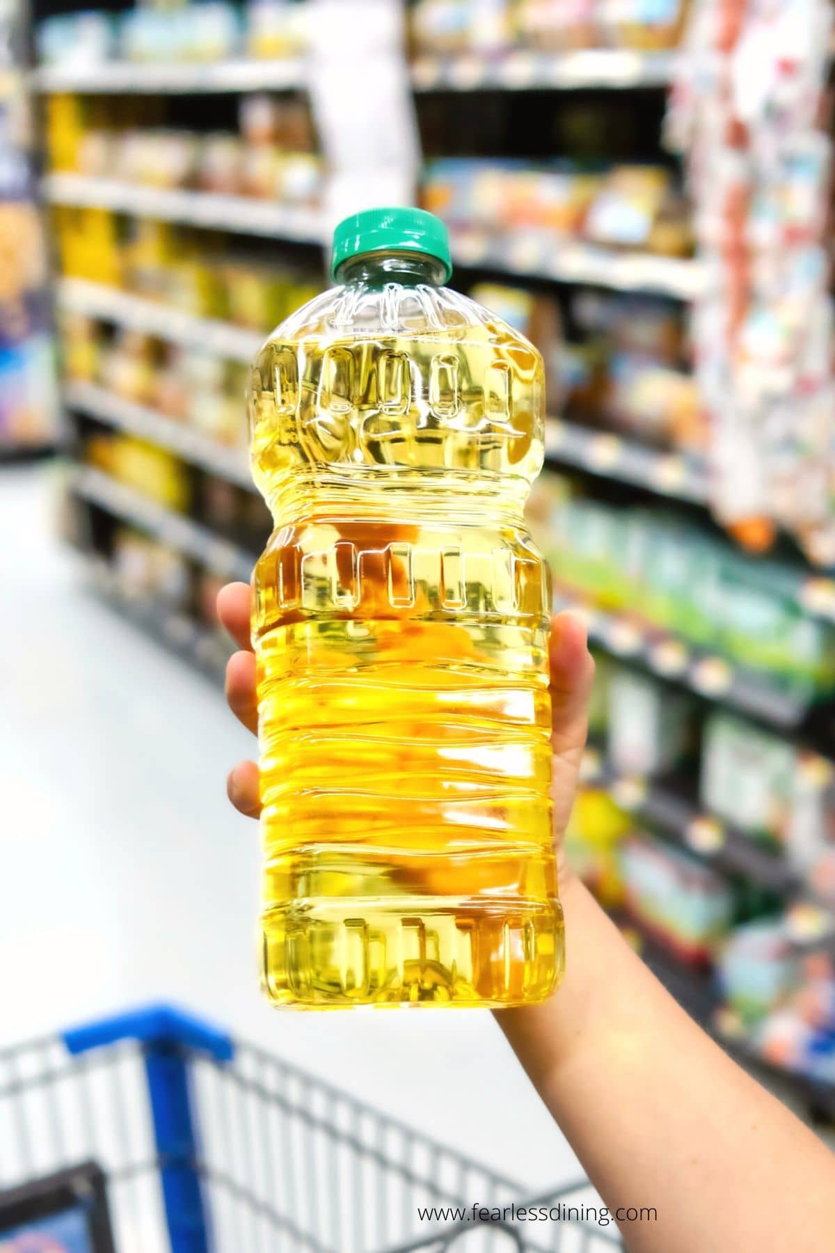 A hand holding up a bottle of cooking oil in the grocery store.