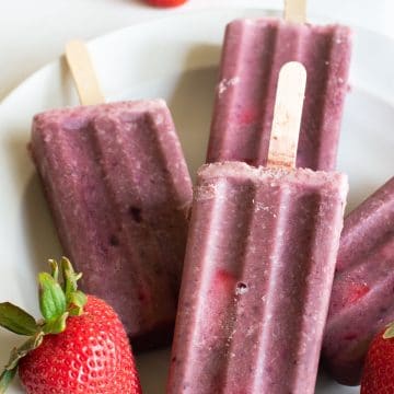 fruity protein popsicles on a plate with fresh strawberries