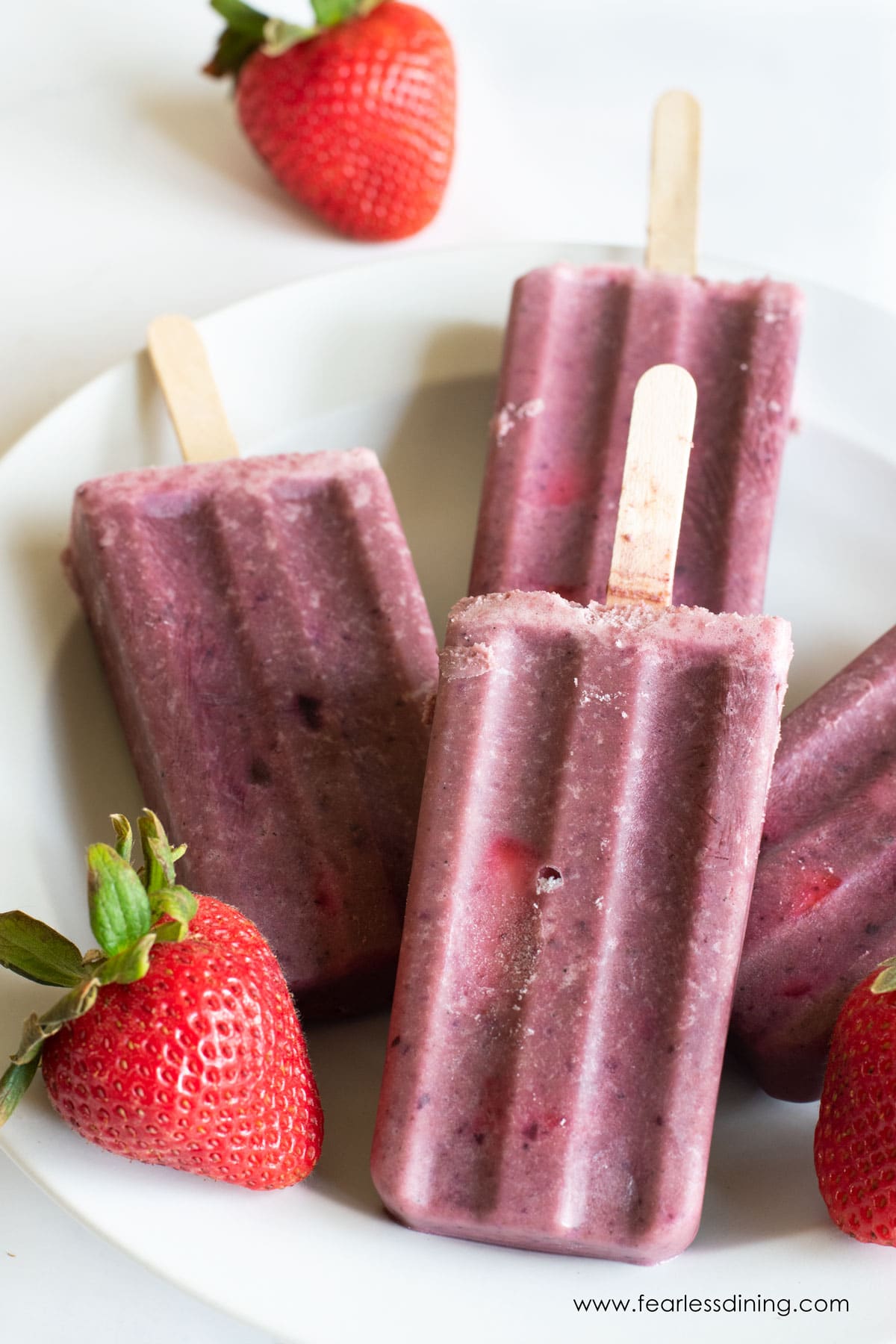 Some fruity protein popsicles on a plate with fresh strawberries.