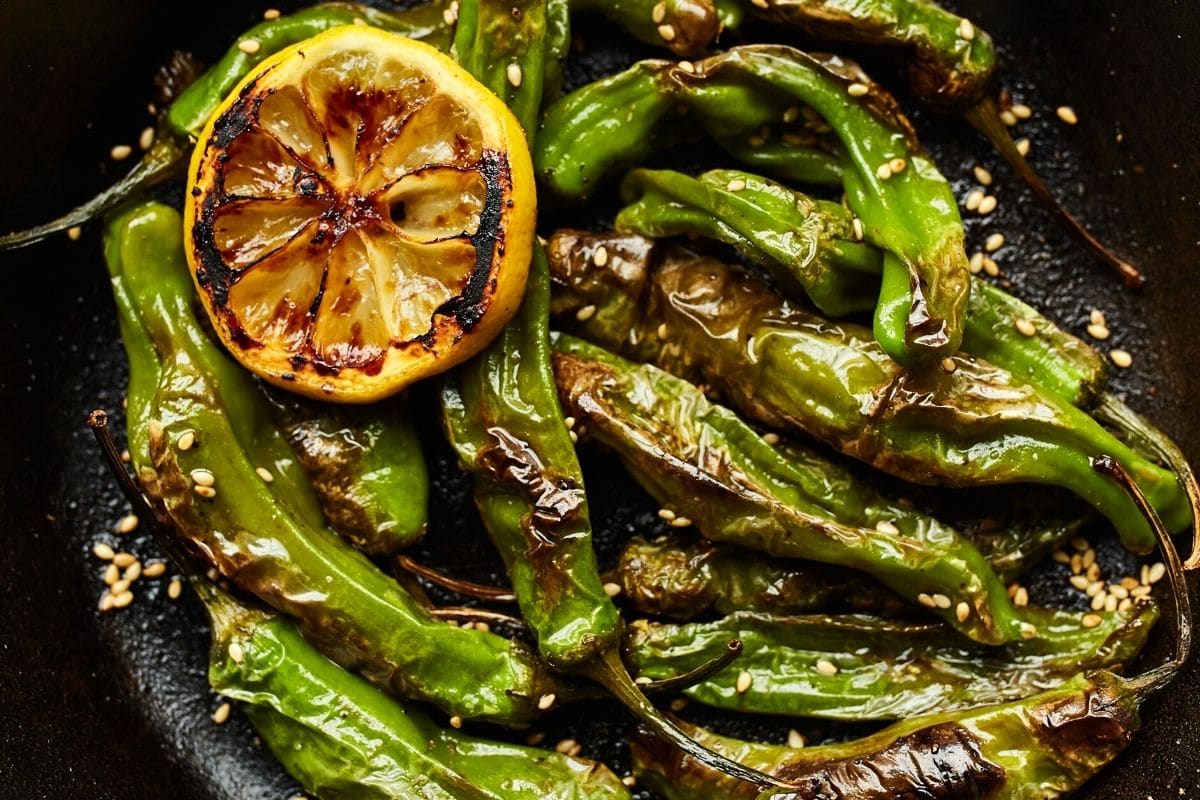 shishito peppers in a skillet with charred lemon.