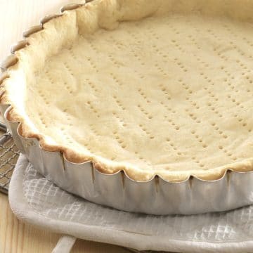 A baked pie crust in a pan. The crust is on a pot holder.