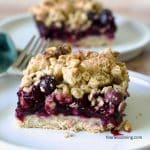 Two blueberry crumble bars on white plates.