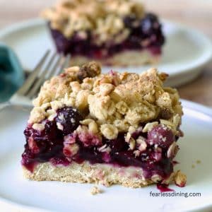 Two blueberry crumble bars on white plates.