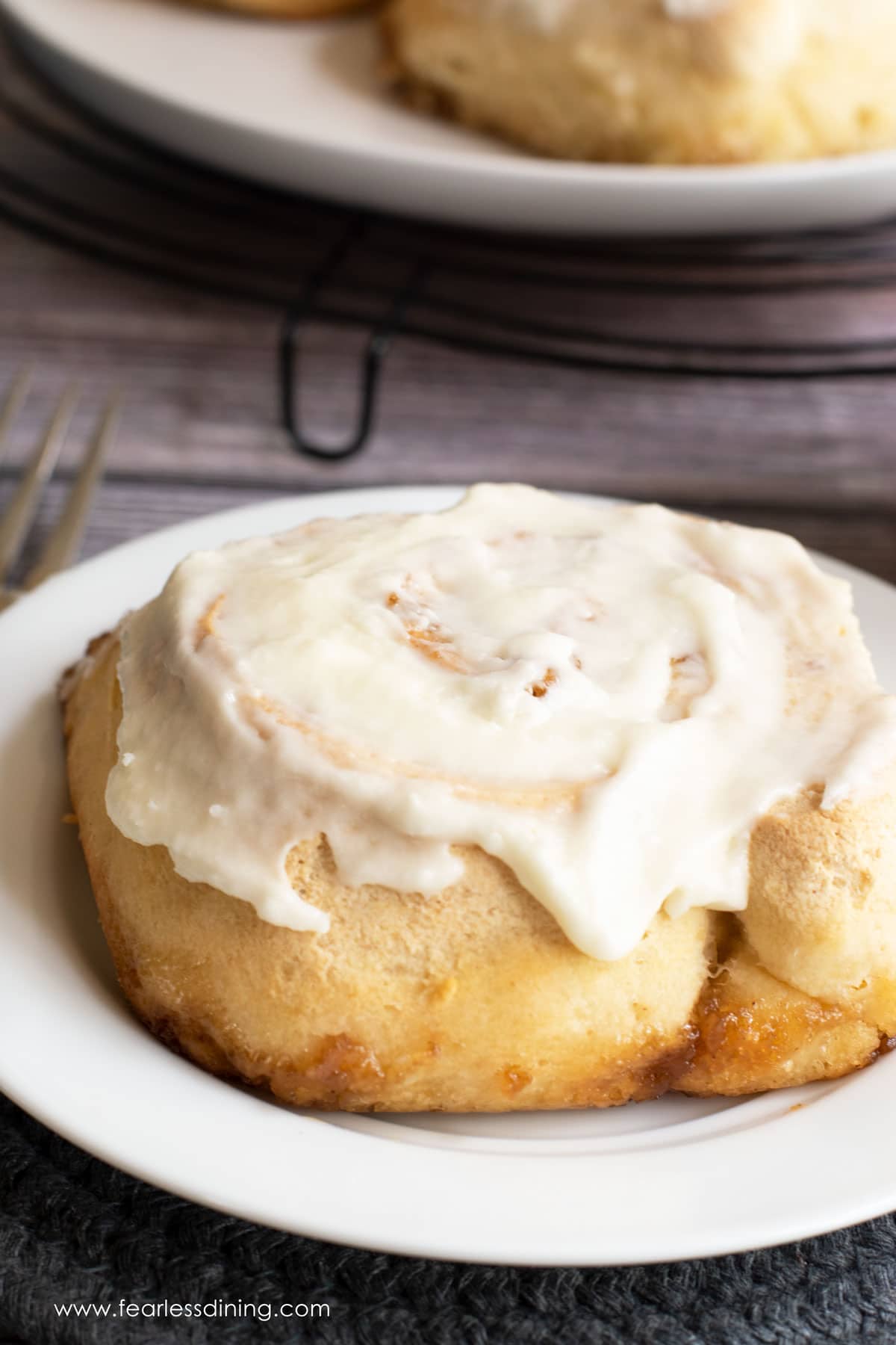 A close up of a gluten free cinnamon roll on a small white plate.