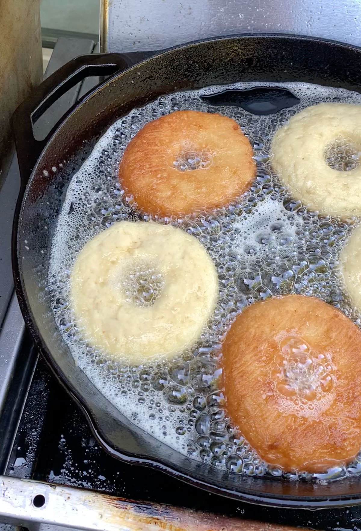 Donuts frying in oil in a cast iron skillet.