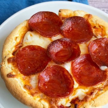 A small deep dish gluten free pizza on a plate. The pizza is topped with pepperoni.