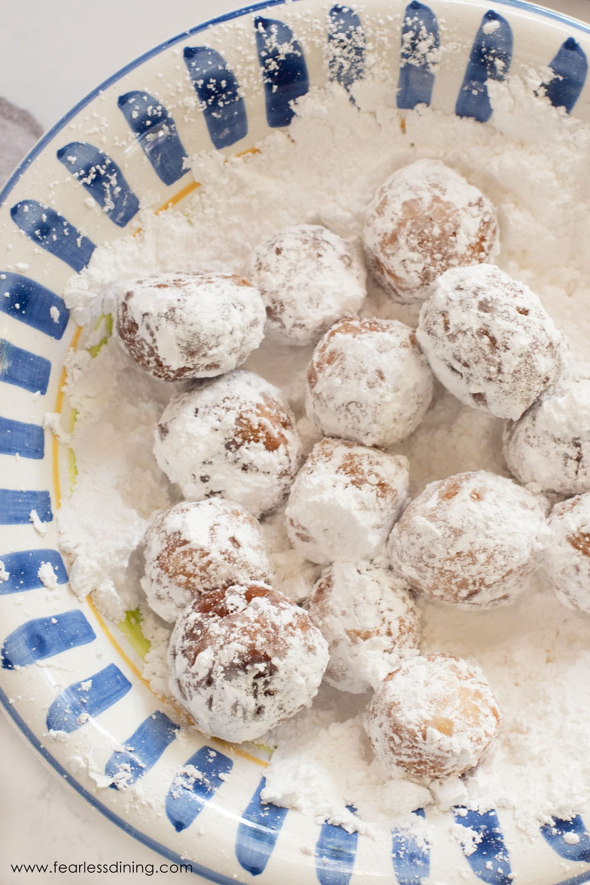 A large bowl filled with powdered sugar. Donut holes are in the sugar.