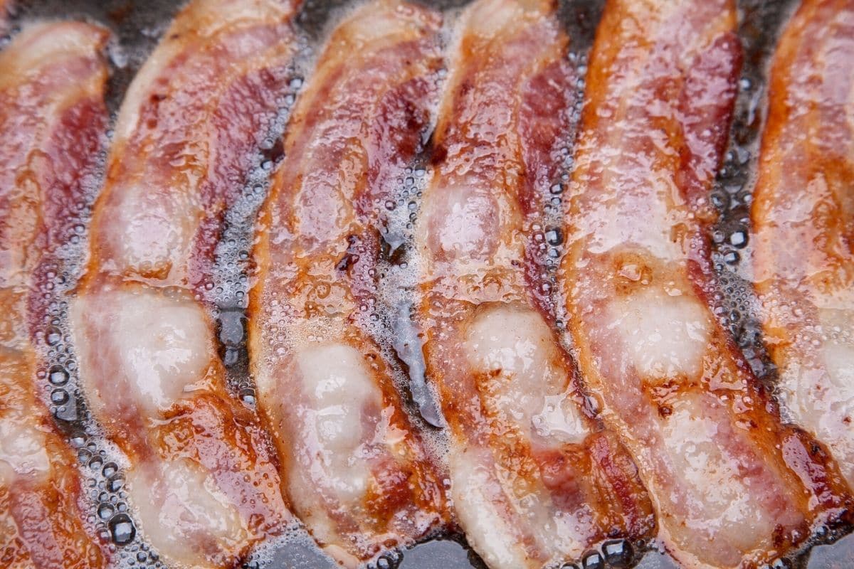 slices of bacon cooking in a skillet.