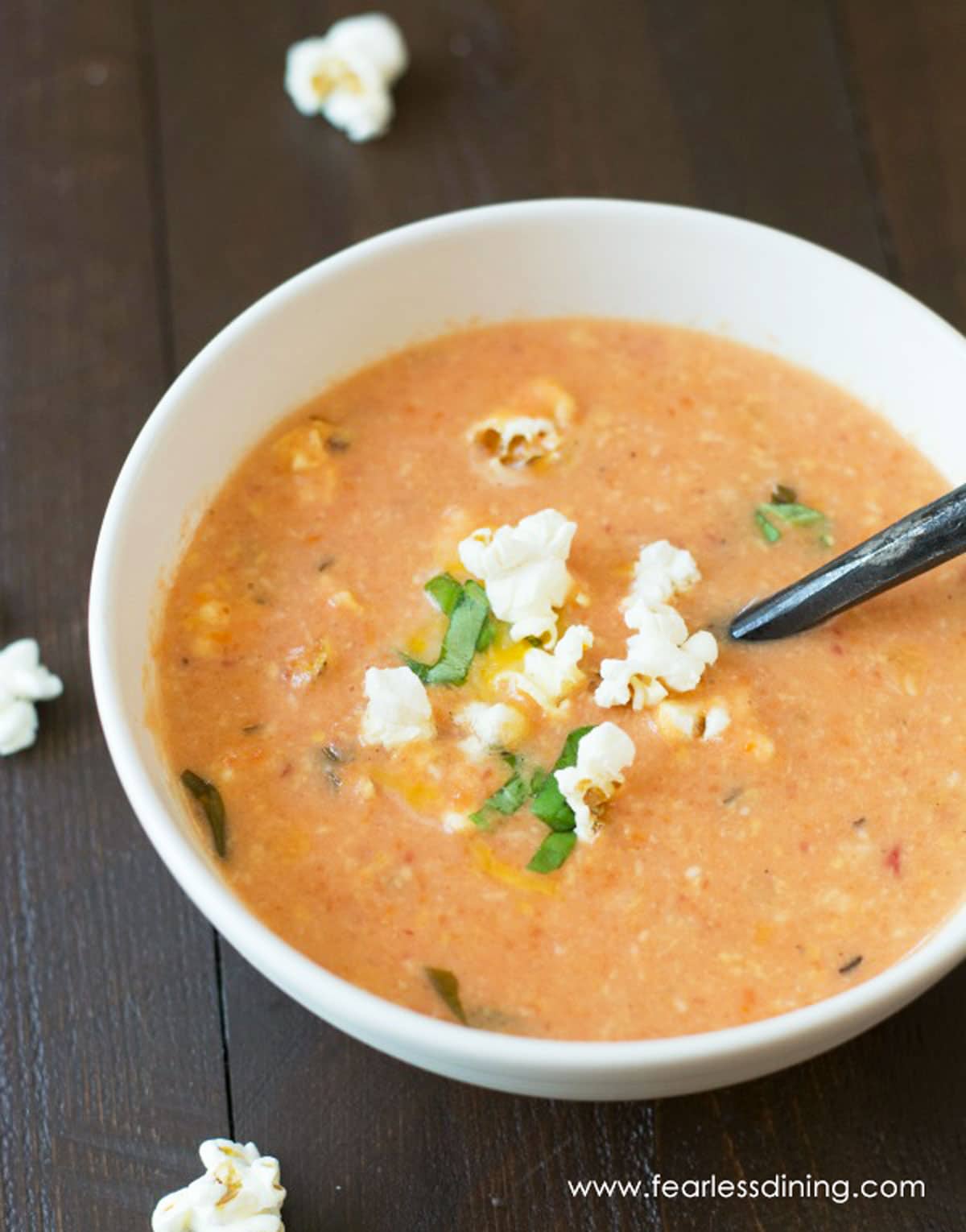 A big bowl of tomato soup. It is garnished with popcorn.