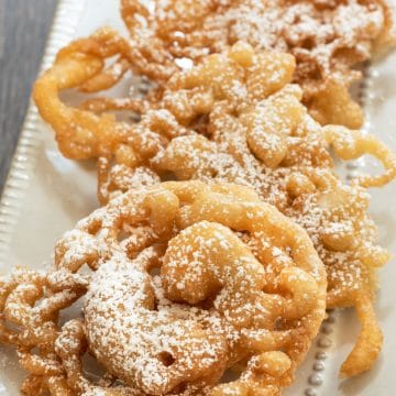 A photo of five sugar dusted funnel cakes on a small platter.