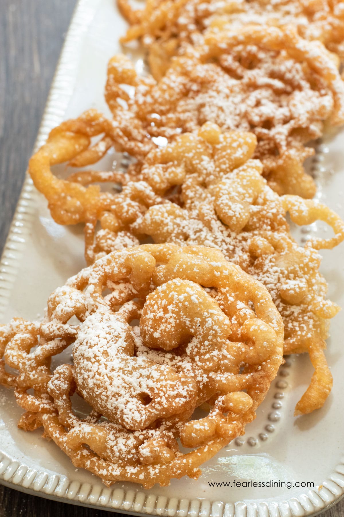 A photo of five sugar dusted funnel cakes on a small platter.