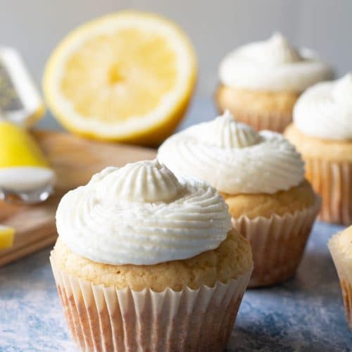 Frosted gluten-free lemon cupcakes next to a cutting board with chopped fresh lemon.