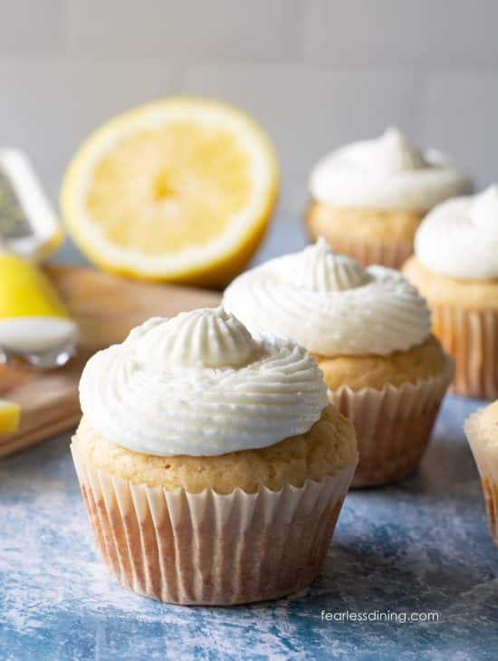 Frosted gluten-free lemon cupcakes next to a cutting board with chopped fresh lemon.