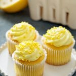 Three lemon cupcakes on a plate. They are frosted and topped with lemon sprinkles.