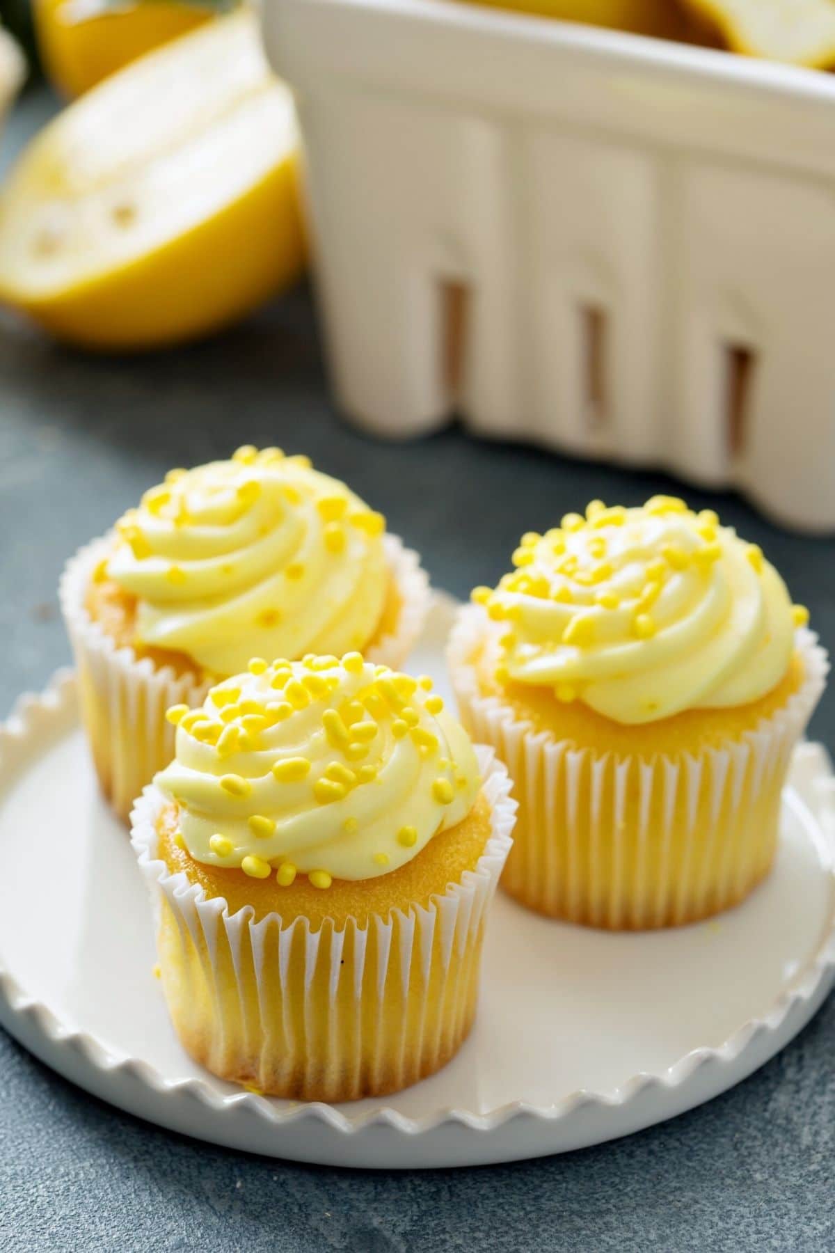 Three lemon cupcakes on a plate. They are frosted and topped with lemon sprinkles.
