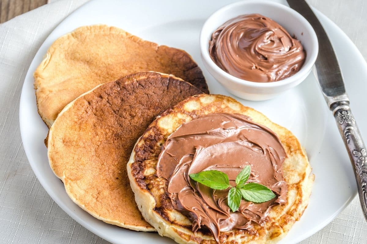 Three pancakes on a plate with Nutella spread on one pancake.